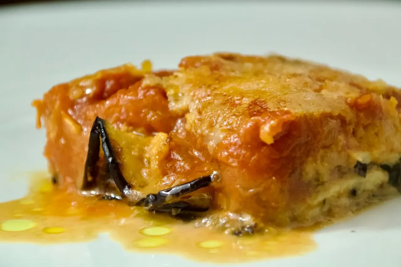 parmigiana di melanzane 01 Primo piano di una fetta di parmigiana di melanzane con strati di salsa di pomodoro, formaggio fuso e melanzane al forno su un piatto bianco, presentata da Giorgio di Cucino di Te, chef a domicilio a Varese.