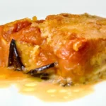 parmigiana di melanzane 02 Primo piano di una fetta di parmigiana di melanzane con strati di salsa di pomodoro, formaggio fuso e melanzane al forno su un piatto bianco, presentata da Giorgio di Cucino di Te, chef a domicilio a Varese.